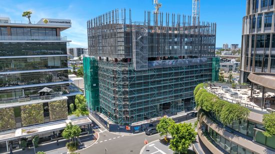 50 First Avenue under construction, situated at a calm intersection near other modern buildings. The large building’s frame is surrounded by scaffolding, and two cranes extend up from behind.