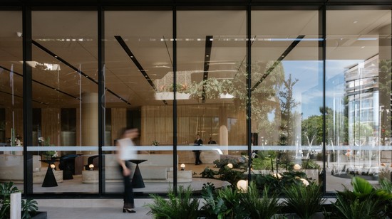 An exterior shot looking inside the lobby at 50 First Avenue. With lush garden beds in the foreground and a tenant walking by on their way to work.