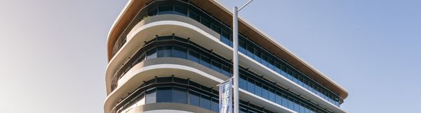 The upper floors of A1 Maroochydore seen from below, with warm sunlight reflecting off its wraparound glass windows.