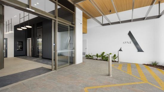 The entrance to A1 Maroochydore’s lobby. A large "A-One" logo is on the wall next to the entrance. The interior of the lobby is styled white with a black feature wall containing the elevators.