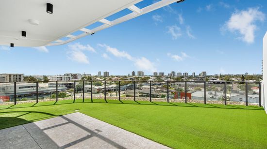The rooftop area of A1 Maroochydore, with a paved area under an awning extending to a grassy open area. Maroochydore can be seen in the distance all around the building through the rooftop’s glass railings.