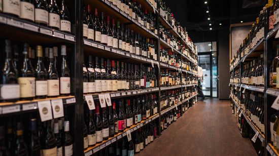 Two long shelves of wine bottles in a bottle shop. Each shelf has a range of styles of wine.