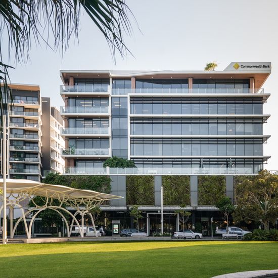 The front of Foundation Place seen from across a neighbouring grassy field. The tall ground floor has a large entrance to the lobby, surrounded by several retailers. Large green walls span the next floor, leading to several floors of modern glass façades. The Commonwealth Bank’s logo is featured on the top right corner of the building.
