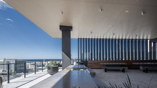 The panoramic rooftop area of Market Lane. Several tables and benches are arranged throughout the space, and Maroochydore and the ocean can be seen in the distance past the glass railings.