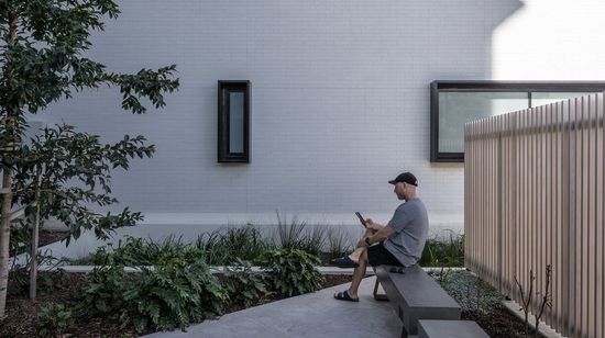 A resident sitting next to a garden area at Market Lane while reading on their phone.