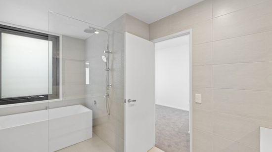 The modern bathroom of an apartment at Market Lane. A shower and separate bathtub are seen through a glass shower divider.