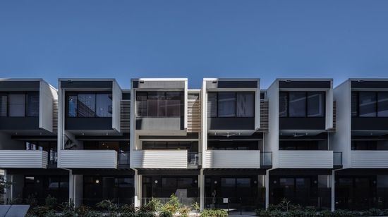 The back of the row of townhouses at Market Lane, showcasing each townhouse’s ground floor patio, second storey balcony and top storey full-height glass windows. The residents’ pool runs along the area below the townhouses.
