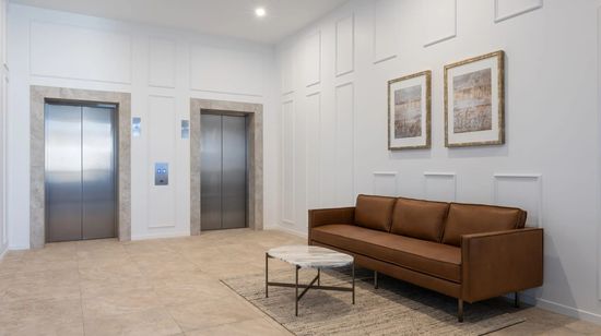 The entrance lobby and elevator bank at The Corso. A designer brown leather couch sits in the lobby beneath abstract artworks.