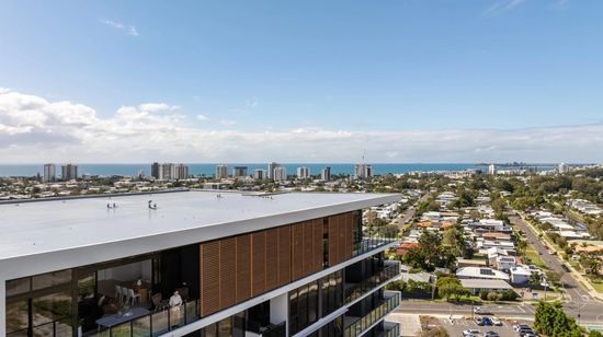 An aerial view of the upper floors of The Corso and the surrounding Maroochydore area. The doors to the penthouse apartment are open with a resident standing on the balcony looking out.
