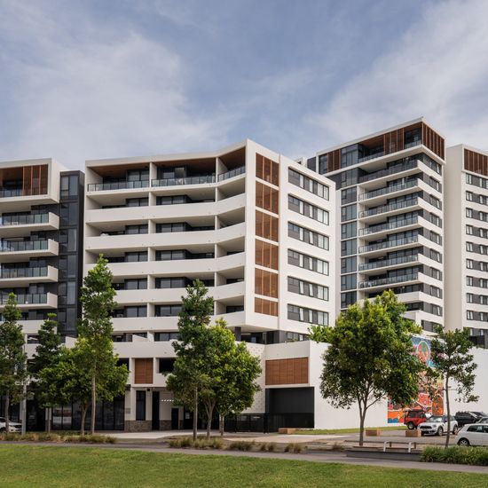 The two apartment buildings of The Corso seen from across a neighbouring grassy field. The towers are white with wooden accents.