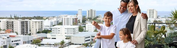 A family of four standing on a balcony looking out over Maroochydore. One of the children is pointing into the distance while their smiling parent look.