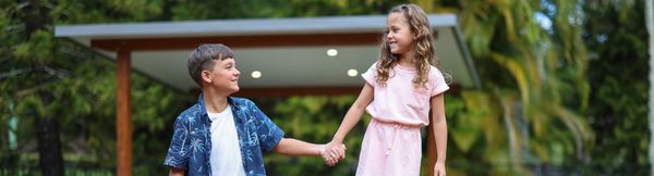 Two children smiling and holding hands in a park surrounded by lush greenery.