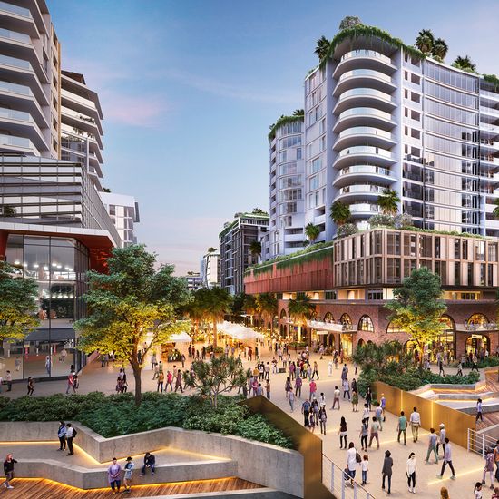An artist’s impression of a public plaza at Maroochydore City Centre running between several modern commercial & retail buildings, with many people walking or seated throughout the plaza.