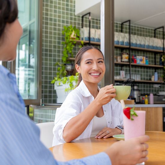 A person smiling while speaking with a friend inside a modern café.