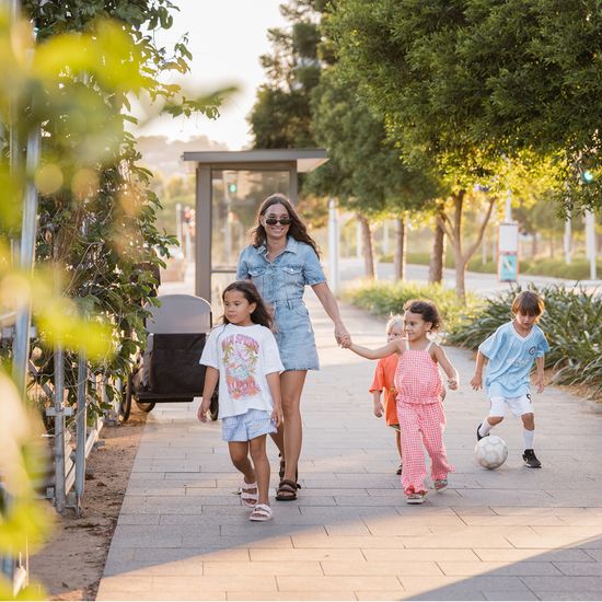 A parent walking with four children through a public area at Maroochydore City Centre, holding one of the children’s hand while another kicks a soccer ball.