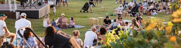 Several families and groups sitting on a lawn around a stage set up for live music.